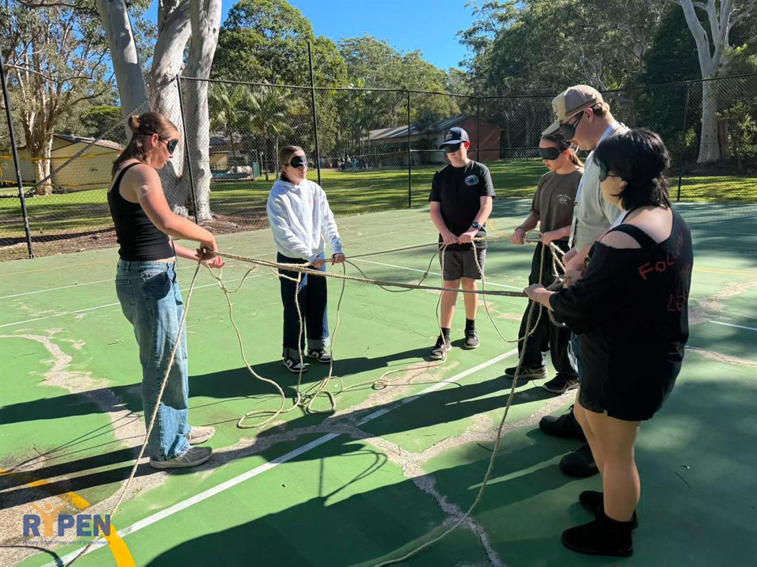 A group working through a rope challenge on the court
